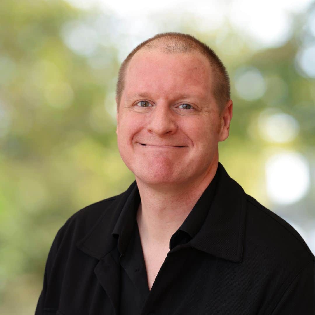 Portrait of smiling man in black shirt. Professional headshot of confident business person with blurred green background.