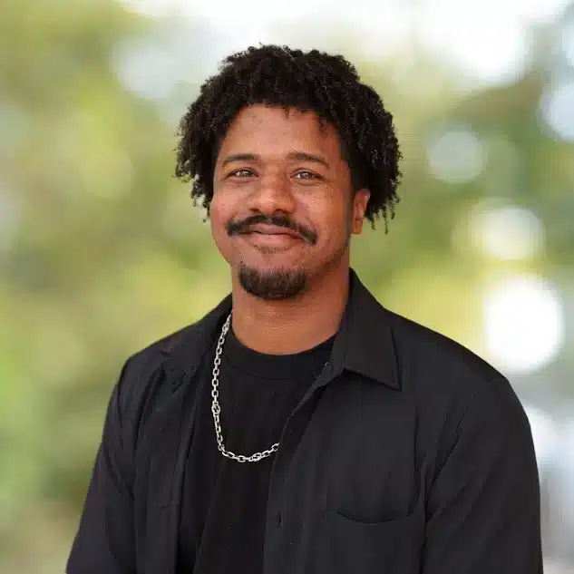 Portrait of a handsome man with Afro hair and a mustache, wearing a black shirt and silver chain.