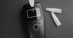 - Bakersfield Recovery Center Handheld breathalyzer with a mouthpiece attached, black body, and two silver-ringed buttons on a dark surface.