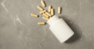 - Bakersfield Recovery Center Pill bottle tipped over with beige capsules spilling onto a gray textured surface on the left side of the image.