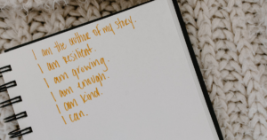Notebook page with orange handwritten affirmations on a knitted beige background of a cozy blanket.