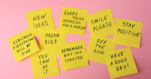 Collection of yellow sticky notes with uplifting phrases on a pink background, like 'New ideas' and 'Dream big'.