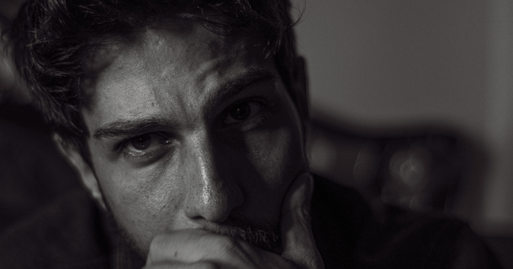 Close-up of a man with a pensive expression, hand resting on his chin, shallow focus background.