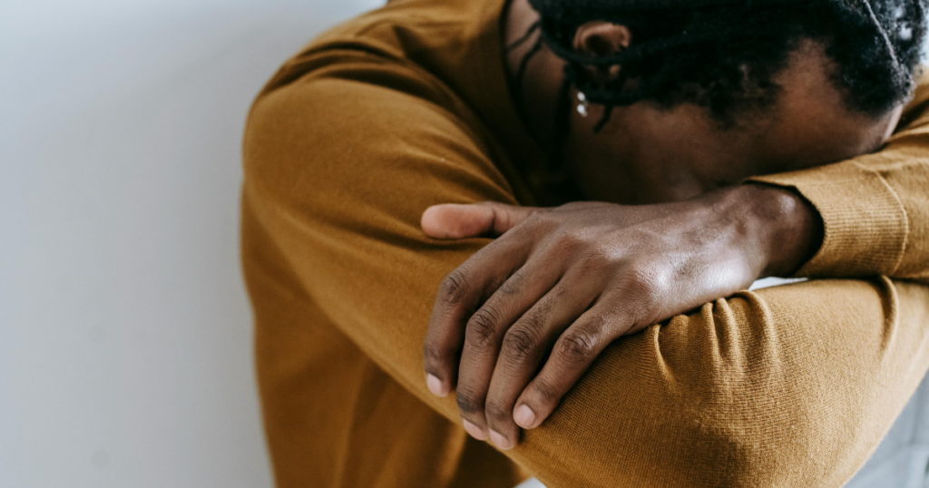 Person in a mustard sweater rests their head on folded arms, conveying tiredness or contemplation.