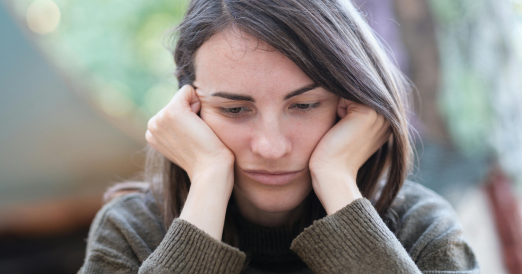 Woman with brown hair resting her face in her hands, looking sad outdoors.